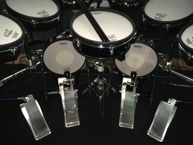A virtuosodrummer.com image of a symmetrical drumset with longboard kick drum pedals and matching longboard hi-hat pedals inc. remote hi-hat cable drives. The foot pedal hardware is made by TRICK Drums USA.
